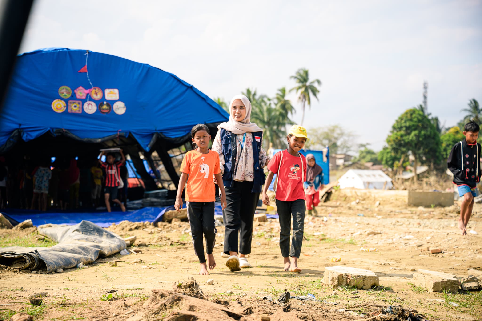A Proyek Pelita volunteer walking with two children through a relief camp